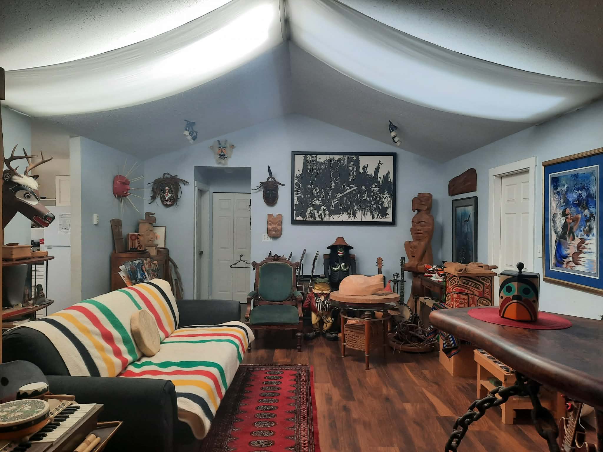 The main gallery room: carved masks, totem figures, prints, and a striped wool blanket couch beneath a vaulted ceiling.